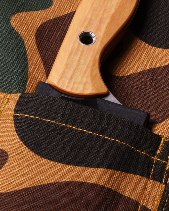 Close-up of a knife with a wooden handle on camouflage-patterned fabric.