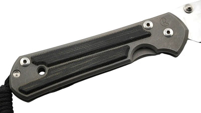 A close-up of a folding knife handle made of dark gray and black textured materials, with a silver metal blade partially visible on a white background.