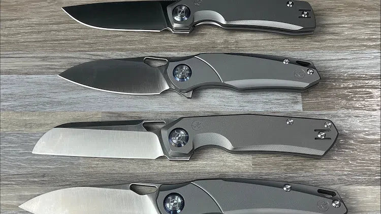Four folding pocket knives with dark gray handles and silver blades arranged horizontally on a gray wood-textured surface.